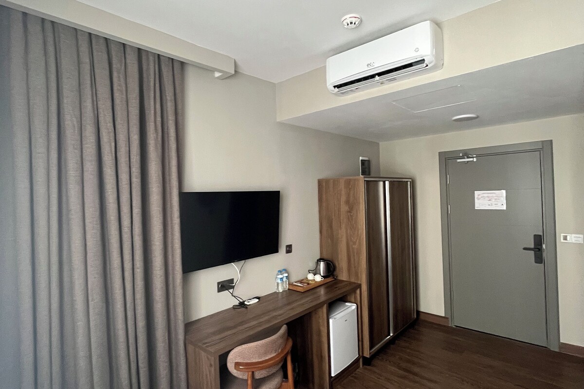 Une chambre d’hôtel avec un bureau en bois, une télévision, un mini-réfrigérateur et une porte sur laquelle est affiché un avis.