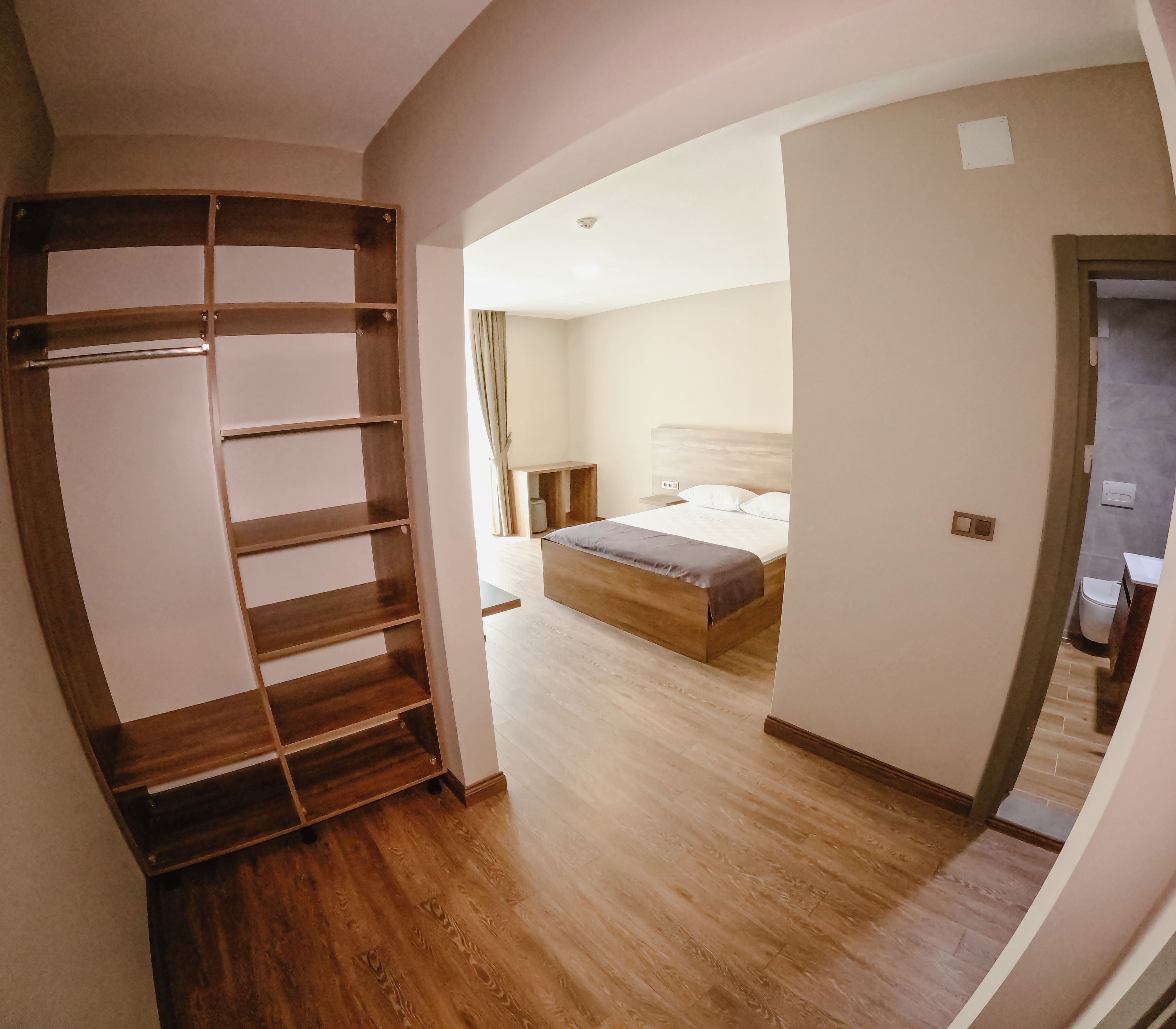 A bedroom with a wooden wardrobe, a bed with a mattress and pillows, and a nightstand.