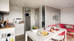 A modern kitchen with white cabinets, a stainless steel refrigerator, and a dining area with a red sofa and a white table. - Water Park for Kids in Valras-plage (Sérignan)
