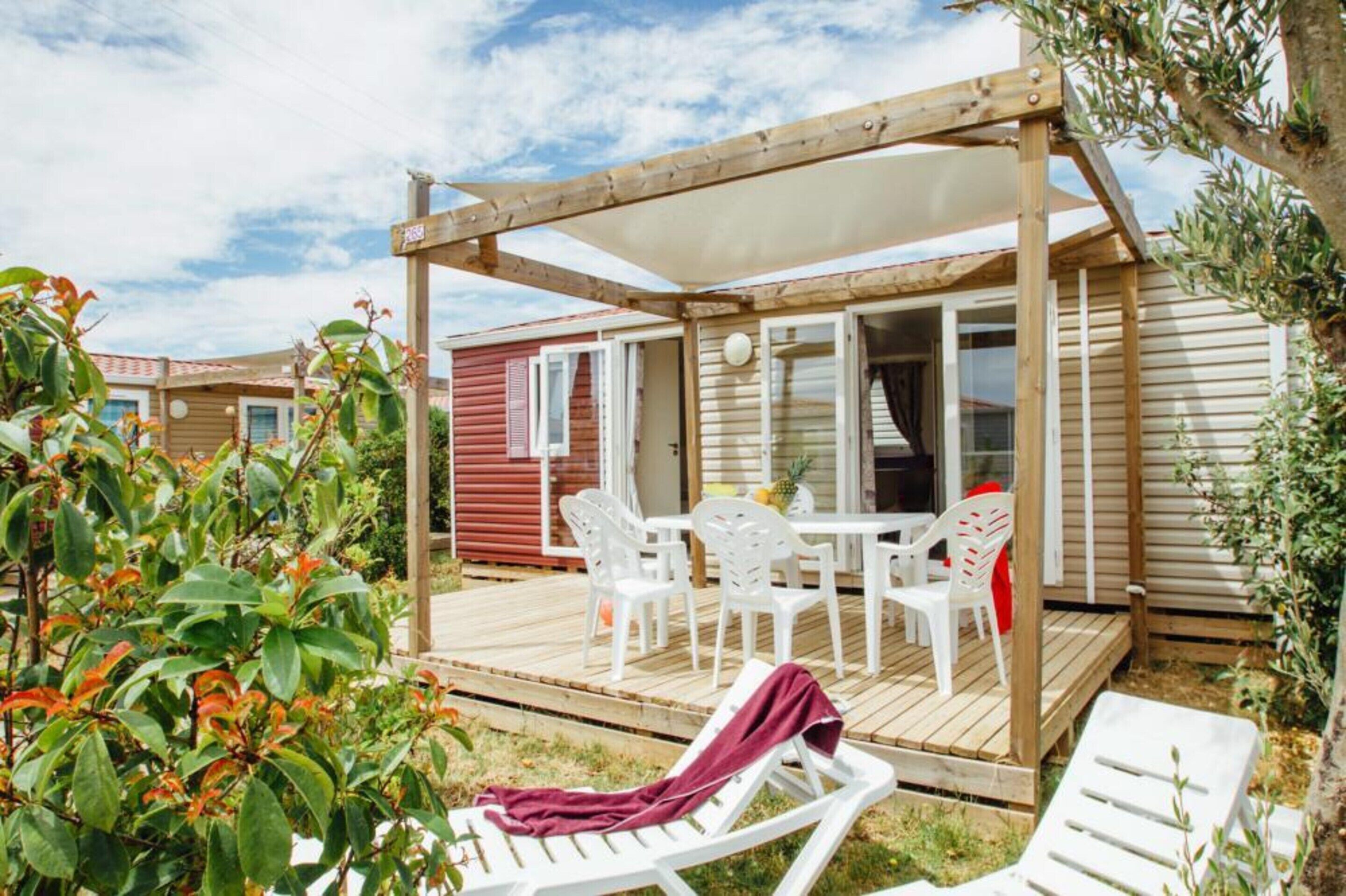 Une terrasse en bois avec une table et des chaises, un espace salon couvert et une vue sur une maison mobile avec une porte rouge.