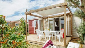 A wooden deck with a table and chairs, a covered seating area, and a view of a mobile home with a red door. - Water Park for Kids in Valras-plage (Sérignan)
