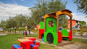 A playground with a green and red play structure, a blue bench, and a red table. - The Garda Village Caravan Park, Sirmione (Sirmione)