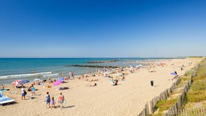 A beach with people sunbathing and swimming, umbrellas, and a wooden fence along the shore. - Sea Stay for Six in Vias Plage (Vias)