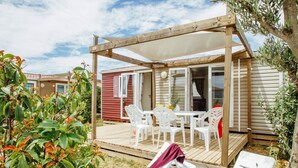 A wooden deck with a table and chairs, a covered seating area, and a view of a neighboring building. - Mobile Home in Bessan With Terrace (Bessan)