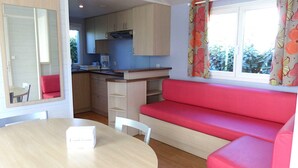 A compact kitchen with a dining area, a red sofa, and a table with a box on it. - Mobile Home in Bessan With Terrace (Bessan)