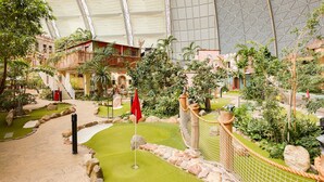 An indoor garden with a golf putting area, surrounded by various plants and a large glass ceiling. - Mobile Home im Tropical Islands Resort (Halbe)