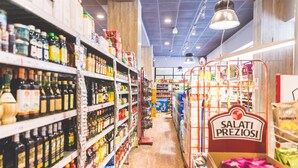 Un pasillo de un supermercado con estantes llenos de varios productos, un letrero que dice 'SALATI PREZIOSI' y una zona de cajas registradoras al fondo.
