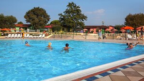 A swimming pool with lounge chairs and umbrellas, surrounded by trees and buildings. - The Garda Village Caravan Park, Sirmione (Sirmione)