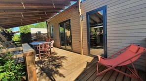 A wooden deck with a table and chairs, a sliding glass door, and a red lounge chair.