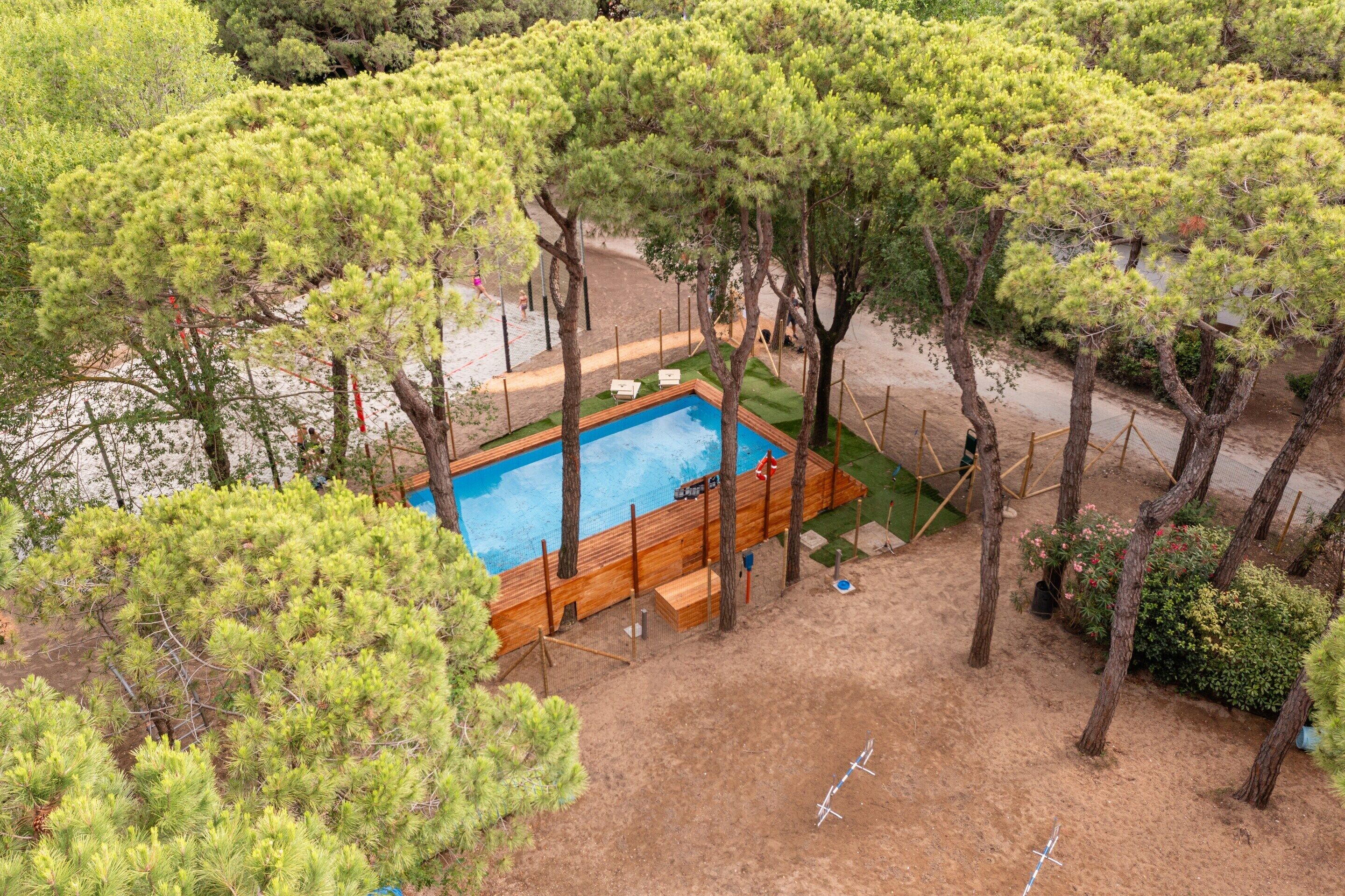 Piscina rodeada por árvores, com um deck de madeira e um banco.