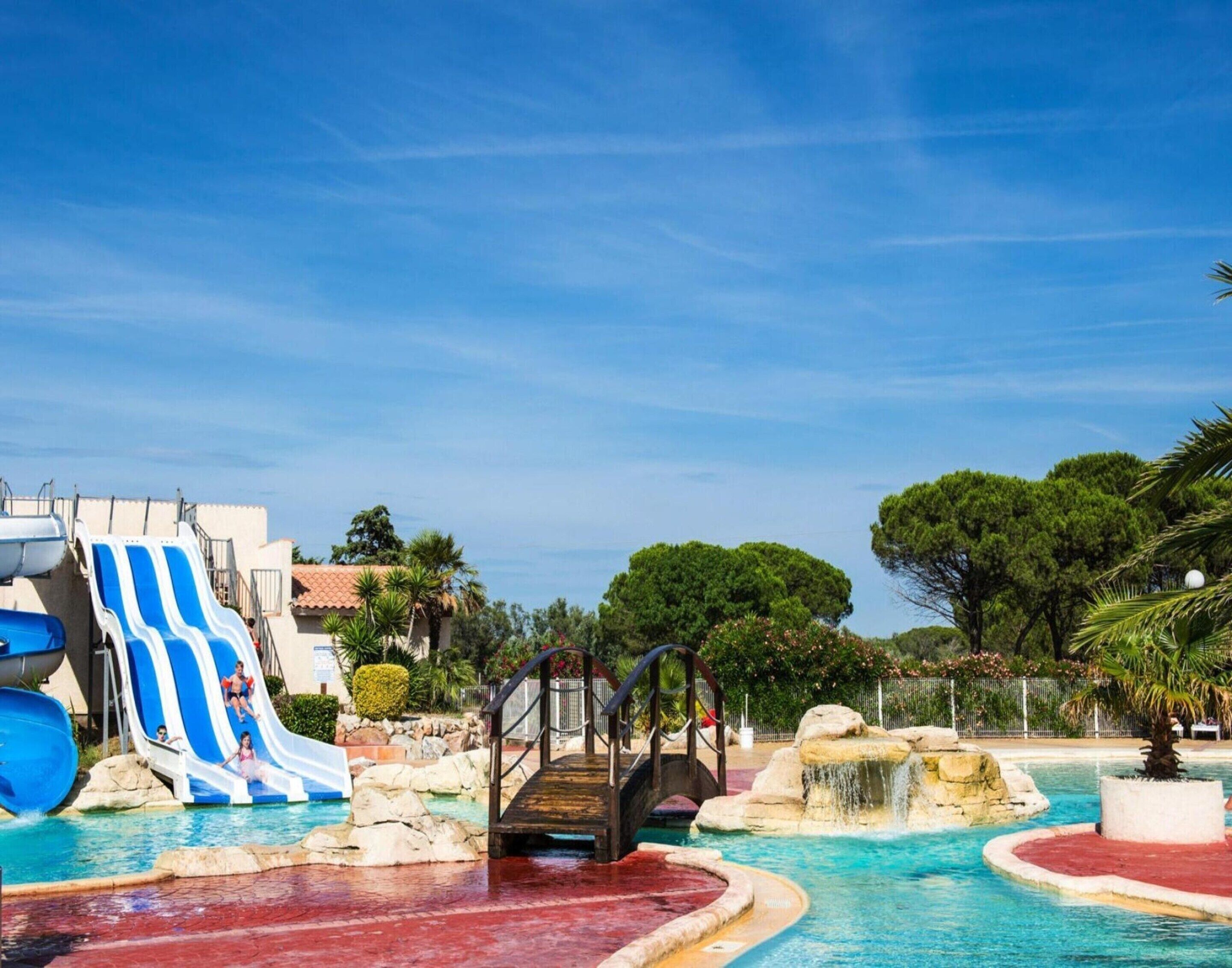A swimming pool with a slide, a bridge, and a rocky water feature.