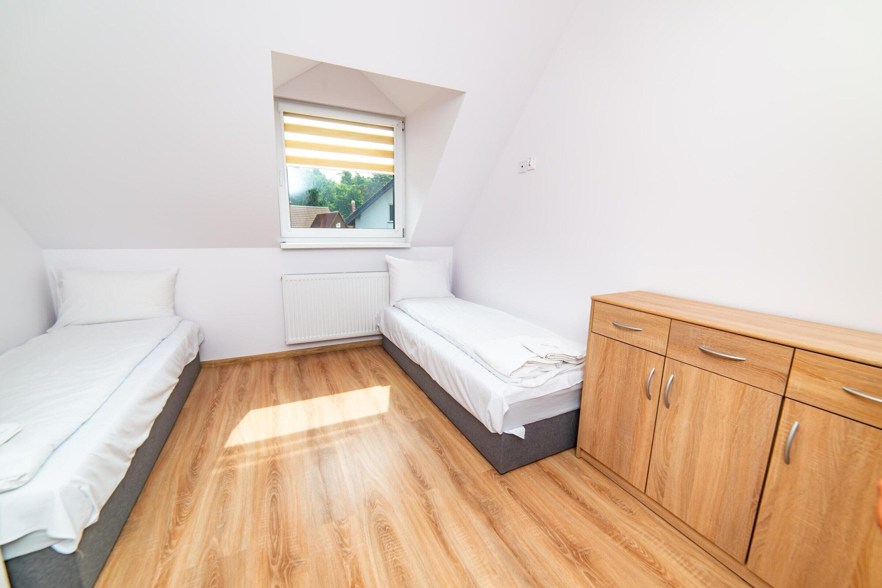 Een ruime, goed verlichte kamer met twee enkele bedden, een houten garderobe en een raam met zonwering.