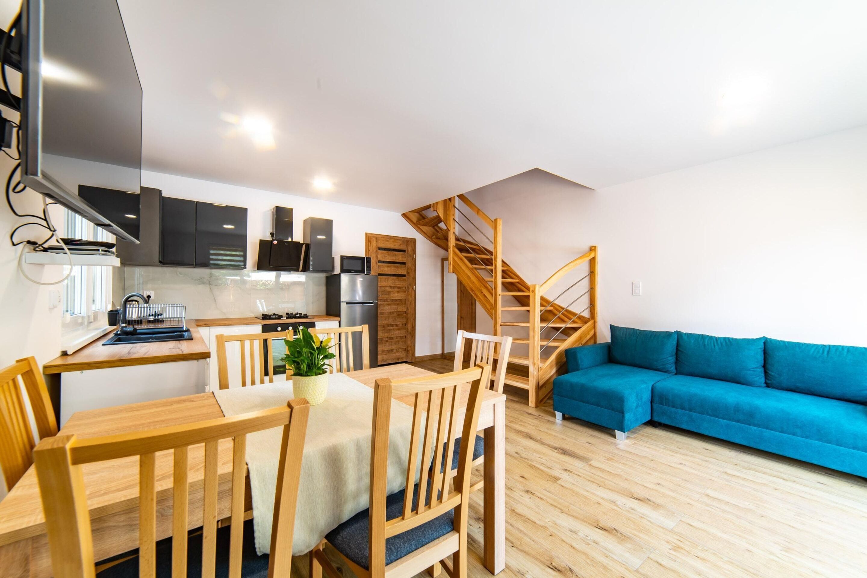 Um espaço de estar moderno com área de jantar, cozinha e escada para um andar superior.