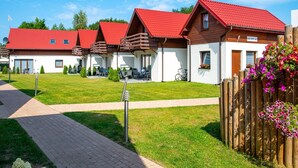 A row of cabins with red roofs, a paved walkway, and a wooden fence with flowers. - 2 Bedroom Holiday Home in Jaroslawiec (Postomino)
