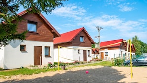 A row of wooden houses with red roofs, a volleyball net, and a sandy ground. - 2 Bedroom Holiday Home in Jaroslawiec (Postomino)