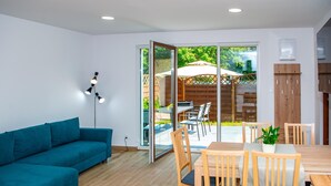 A modern living room with a teal sofa, wooden dining table, and chairs. - 2 Bedroom Holiday Home in Jaroslawiec (Postomino)