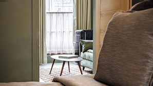 Una habitación con cama, una mesita y un sofá. Se aprecia una ventana con cortinas y vistas a edificios.