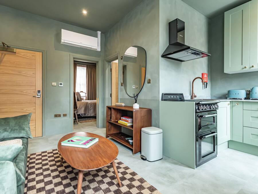 A compact living space with a kitchenette, a wooden door, a mirror, and a small table with a book.
