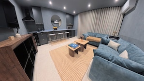 Una sala moderna con un sofá azul, una mesa de centro de madera y una cocina con estufa y lavaplatos.
