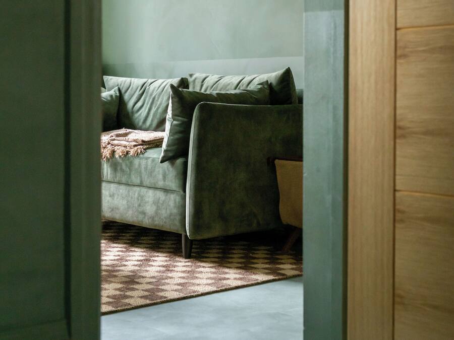 Una habitación con un sofá gris, un tapete estampado y una puerta de madera.