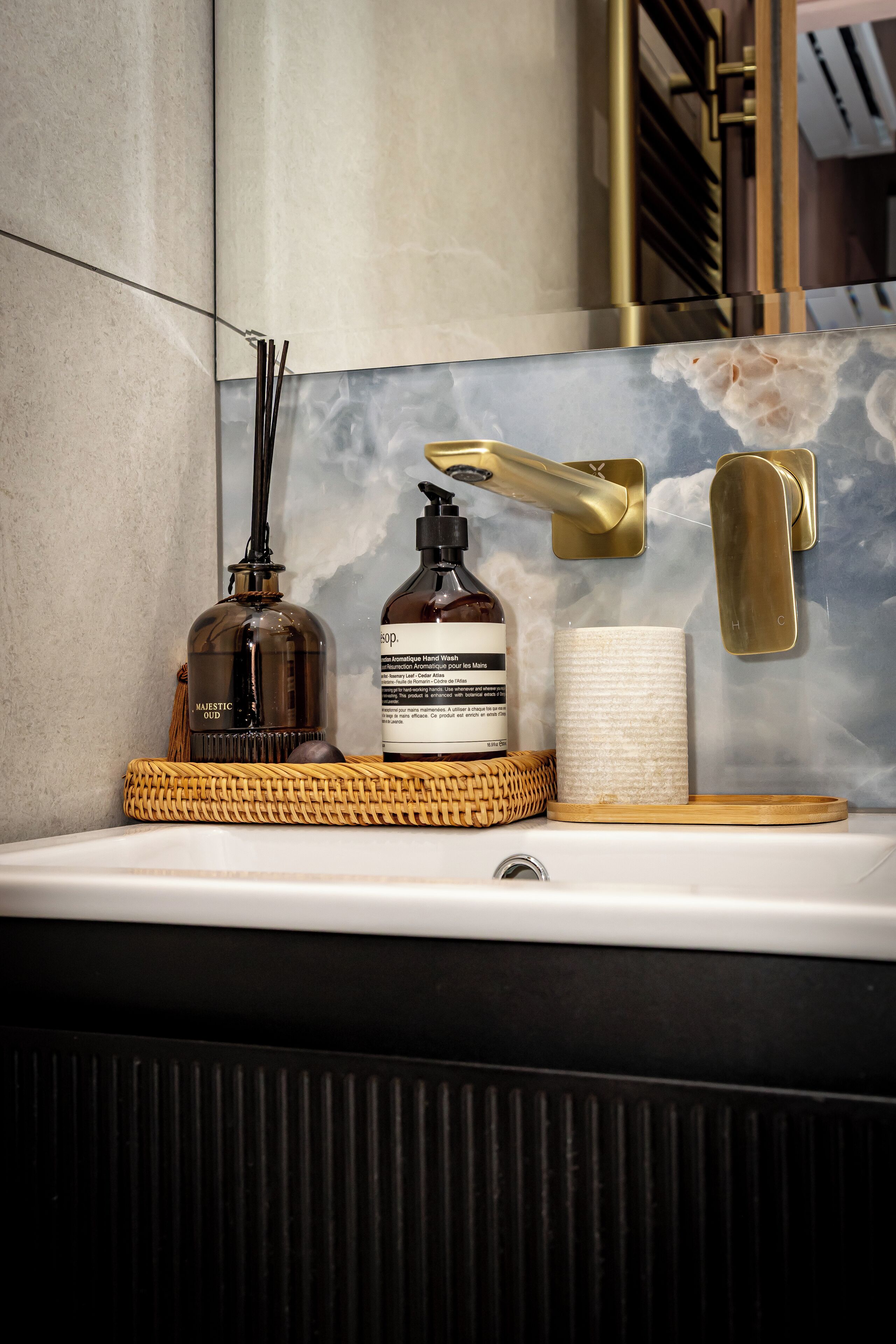 A bathroom vanity with a marble backsplash, a gold faucet, and two bottles of hand soap.