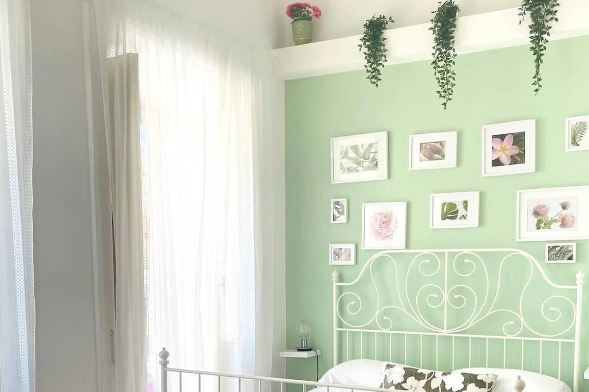 Un dormitorio con estructura de cama metálica blanca, una mesita de noche pequeña y una pared decorada con cuadros.