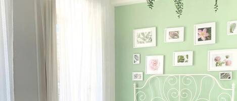 Un dormitorio con estructura de cama metálica blanca, una mesita de noche pequeña y una pared decorada con cuadros.