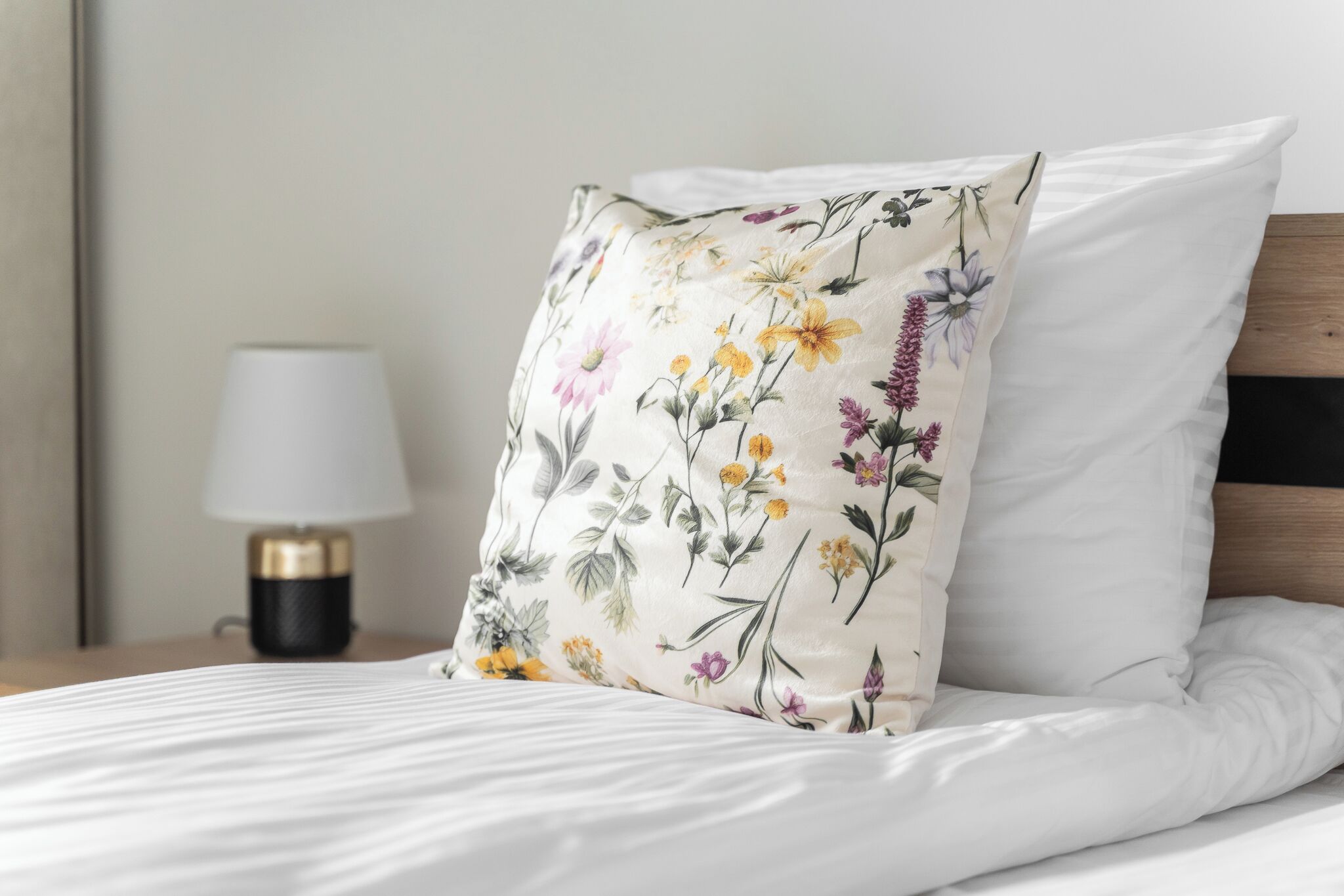 A neatly made bed with a floral pillow and a bedside lamp on a wooden nightstand.