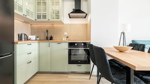 A modern kitchen with light green cabinets, a wooden countertop, and a black stove. - MARGI Verde Apartament (Szczecin)