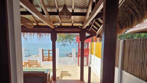 Un pasillo de madera que conduce a una zona de playa con una estructura de techo de paja, un banco y vistas al mar.