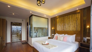 Quarto de hotel moderno com uma cama grande, banheiro envidraçado e detalhes em madeira, incluindo painéis e piso.