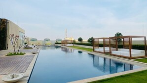 Une piscine moderne dotée d’une terrasse en bois et de chaises longues, entourée d’une pelouse bien entretenue et de quelques arbres.