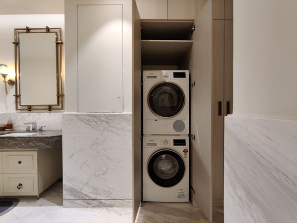 A modern bathroom with a marble sink, a mirror with a gold frame, and stacked washing machines.