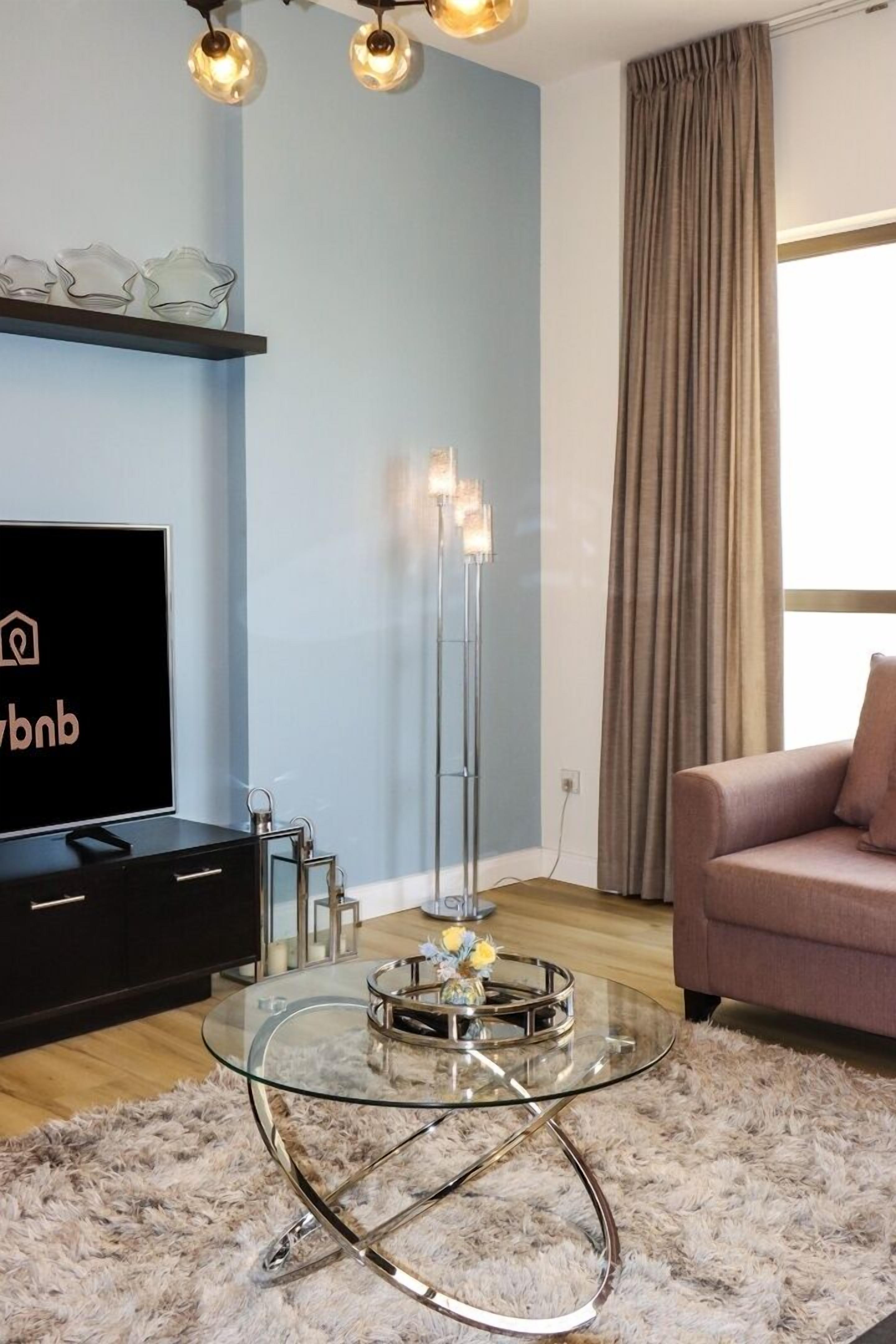 A modern living room with a glass coffee table, a flat-screen TV, a sofa, and a tall floor lamp.