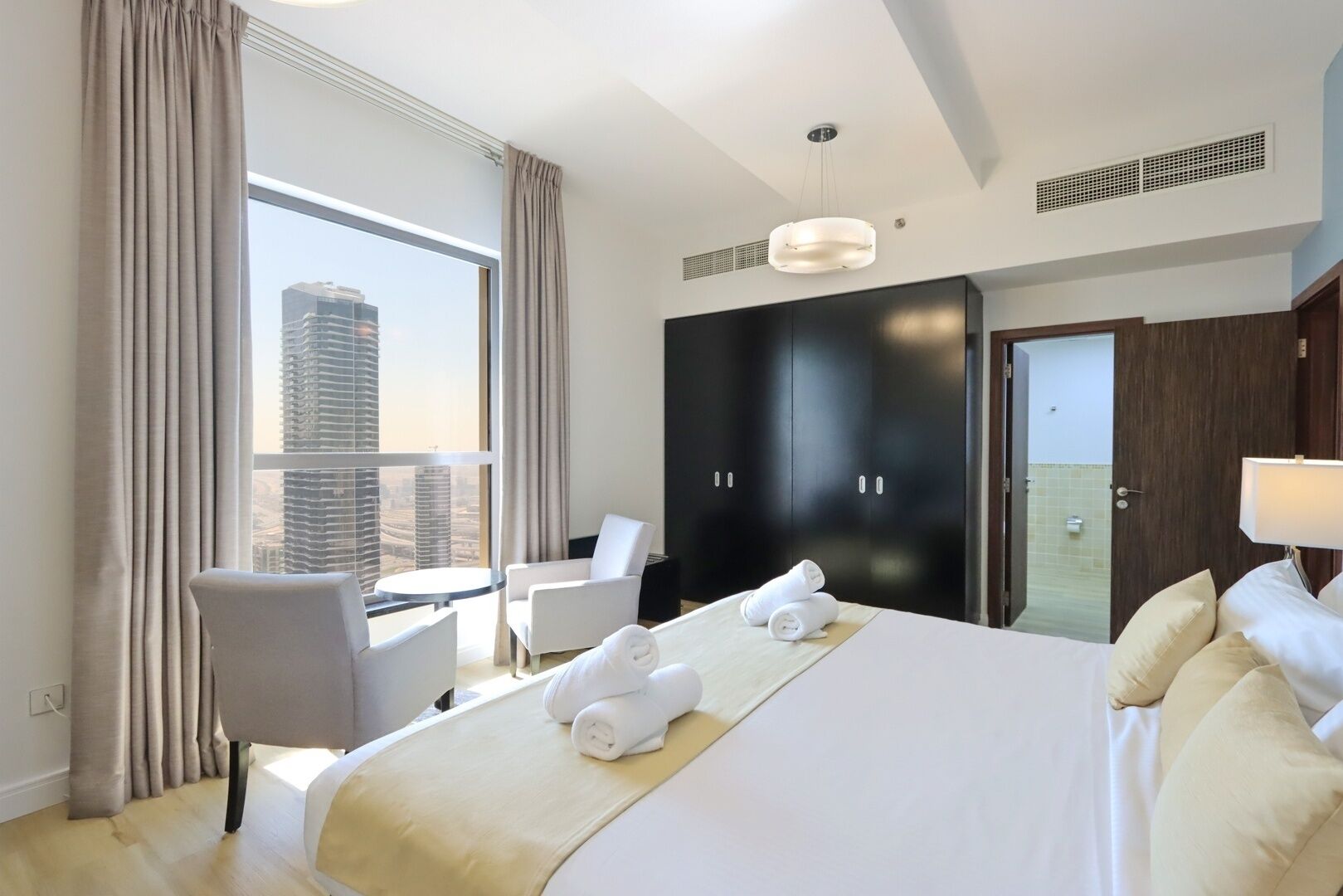 A hotel room with a large bed, two chairs, a desk, and a view of a cityscape.