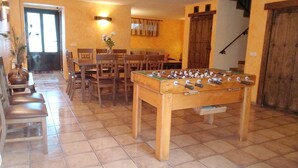 A room with a foosball table, wooden chairs, a dining table with chairs, and a staircase.