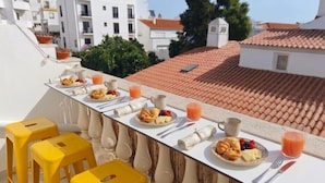Un balcón con una mesa para el desayuno, que incluye platos de comida y bebidas, además de taburetes amarillos.