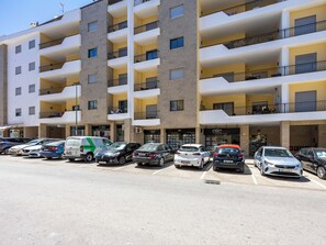 A multi-story residential building with balconies, a parking lot, and several cars.