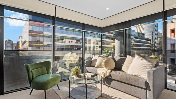 A modern living room with a green armchair, a grey sofa, and a glass coffee table.