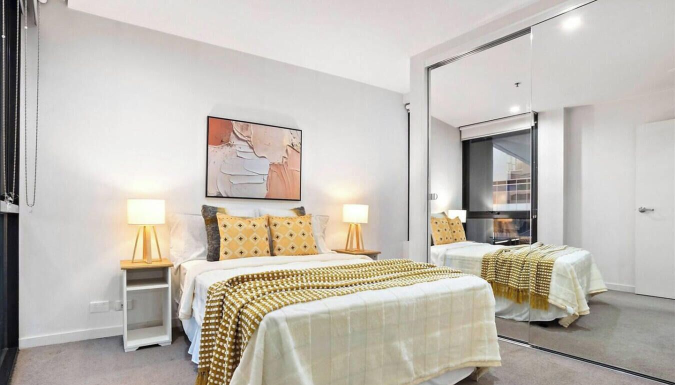 A modern bedroom with two beds, a large mirror, and a painting on the wall.