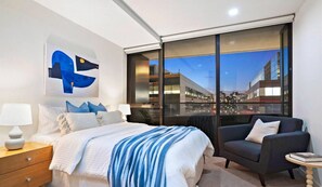 A modern hotel room with a large bed, a seating area, and a city view through floor-to-ceiling windows. - Serrata - 2B2B Docklands with CP (Docklands)
