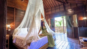A room with a bed under a canopy, wooden walls, a small table, and a view of the outdoors. - The Dukuh Retreat (Tabanan)