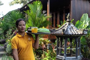 A person in a yellow shirt carrying a tray with a beverage and a food item. - The Dukuh Retreat (Tabanan)