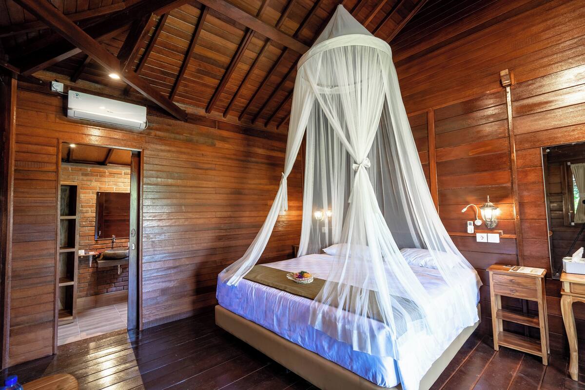 A wooden room with a bed under a canopy, a small table, and a mirror on the wall.