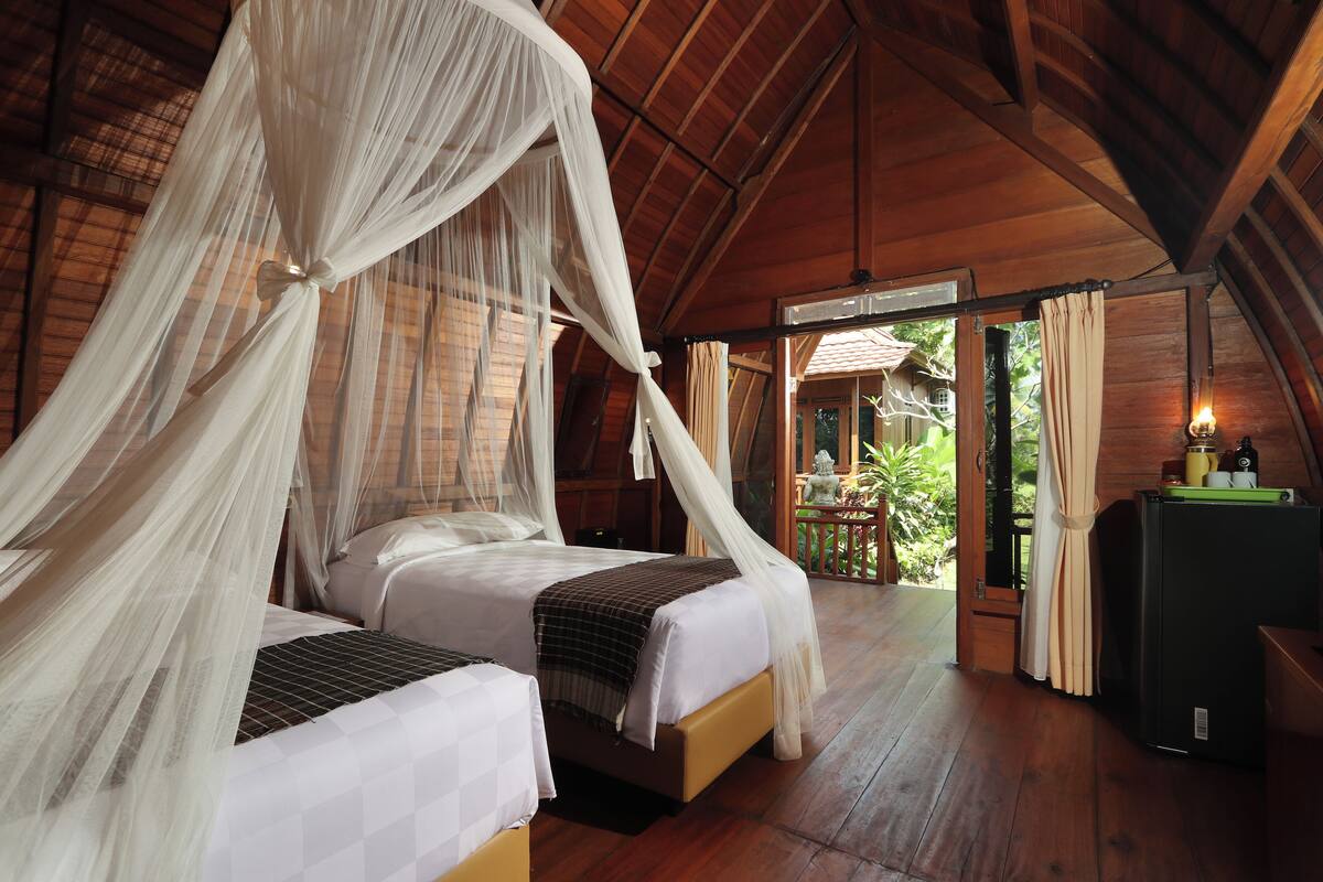 A room with two beds, a wooden ceiling, and a view of the outdoors.