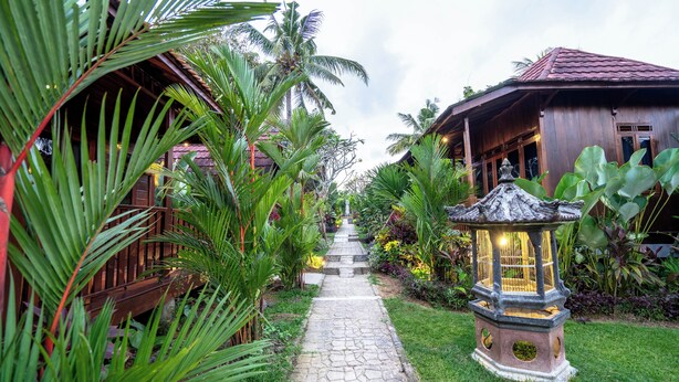 A stone pathway leading to a traditional wooden building with a tiled roof, surrounded by lush tropical vegetation. - The Dukuh Retreat (Tabanan)