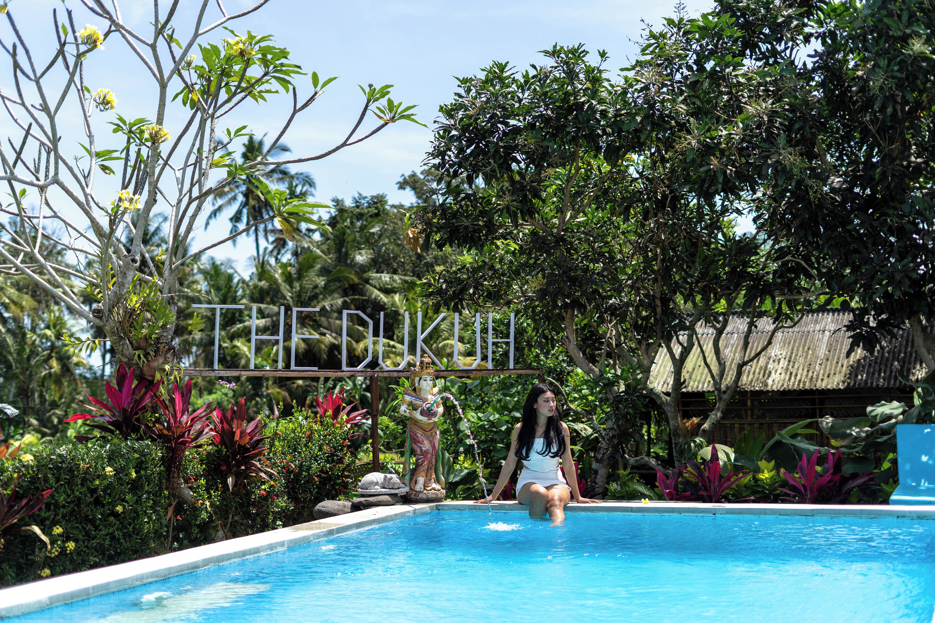 A swimming pool with a statue, surrounded by lush greenery and a tropical setting.