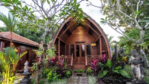 A wooden building with a porch, surrounded by lush tropical plants and a statue. - The Dukuh Retreat (Tabanan)