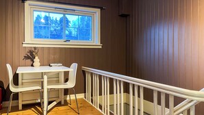 A room with a wooden floor, a white table with two chairs, a window with a view of trees, and a white railing. - JX Homestay (Ringerike)