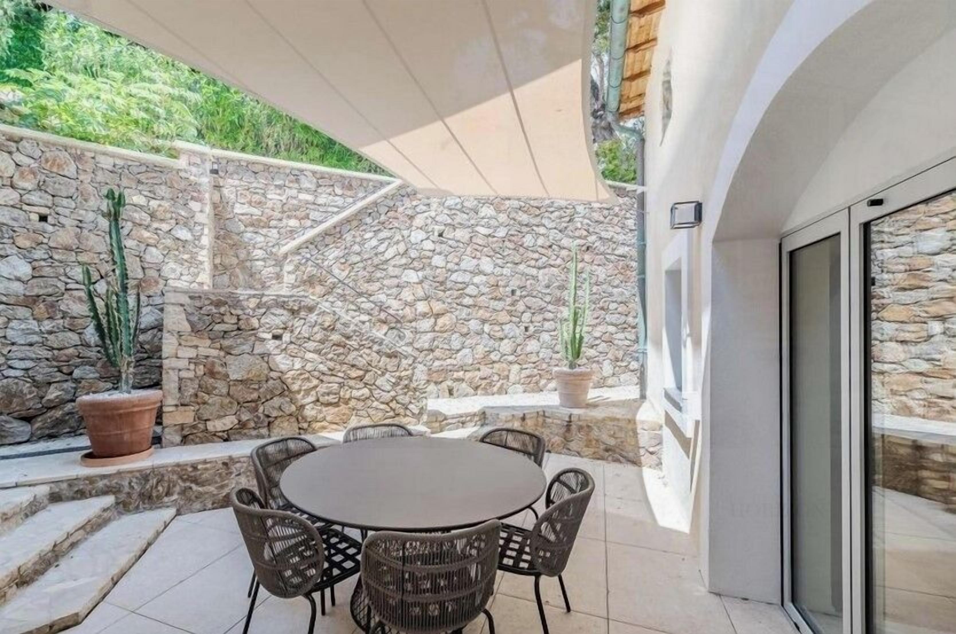 Eine Terrasse im Freien mit einer Steinmauer, einem runden Tisch und Korbstühlen.